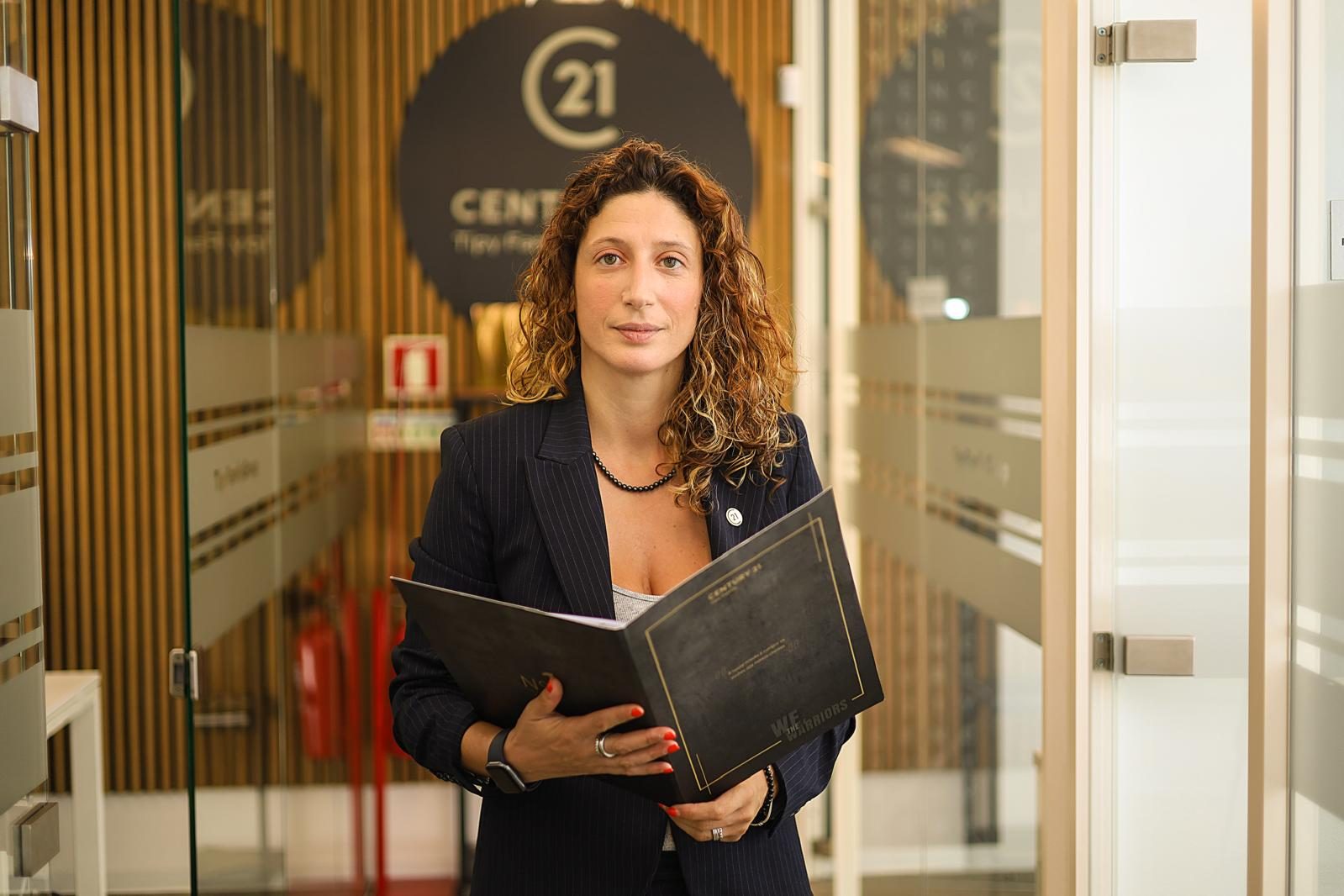 Consultora imobiliária de fato risca-de-giz com pasta corporativa, em corredor de escritório, fotografia de Daniel Robles
