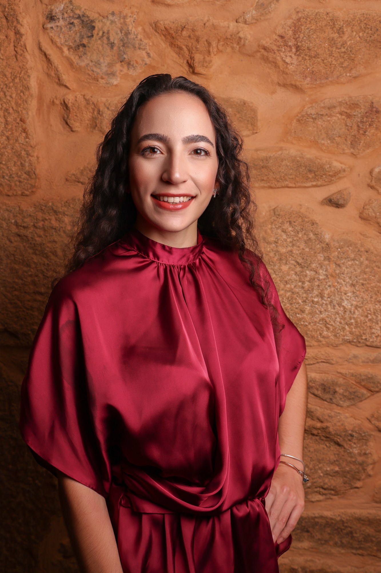 Retrato profissional de empresária de vestido bordeaux, de meio corpo, junto a parede de pedra, fotografia de Daniel Robles