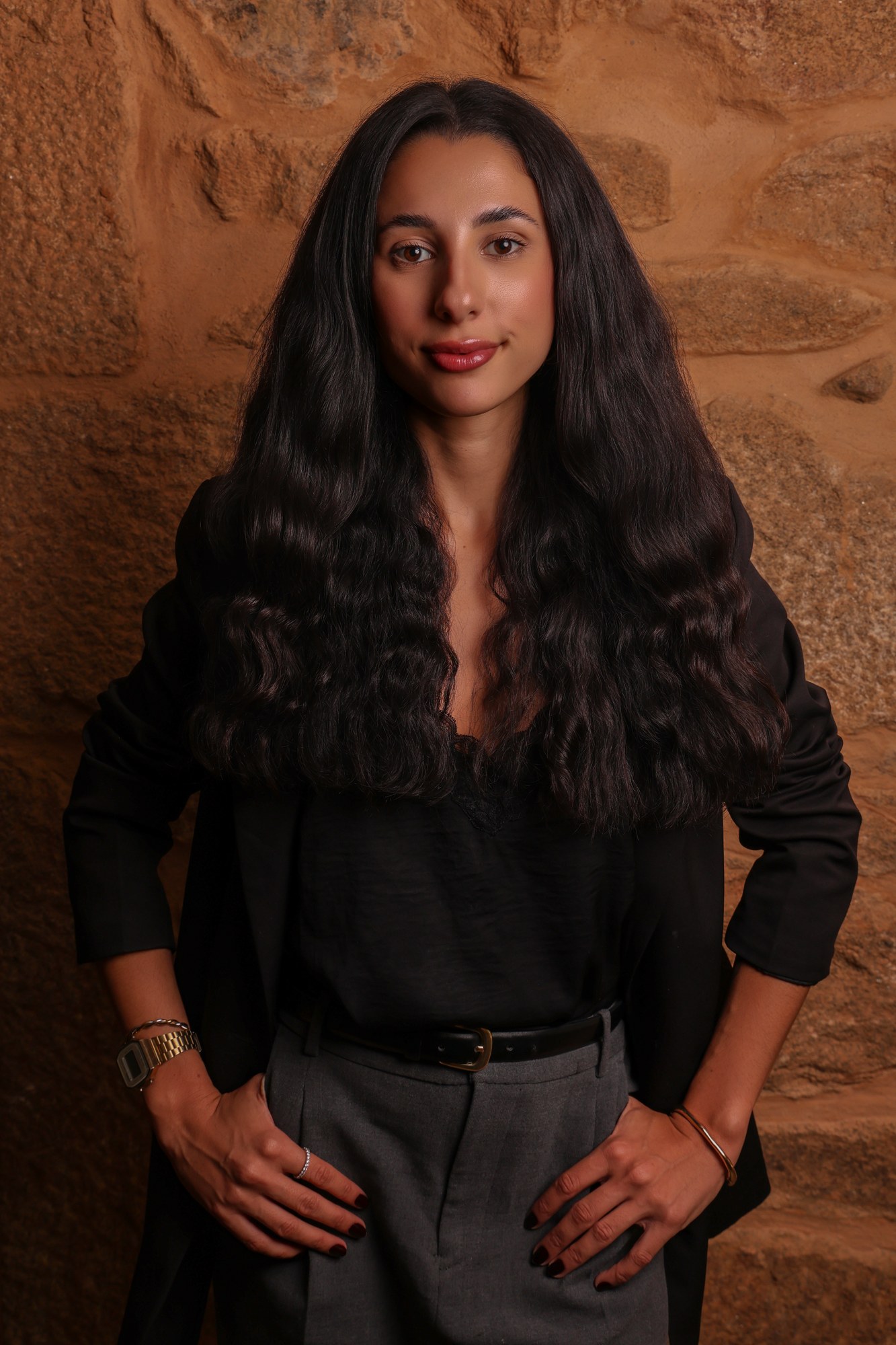 Retrato profissional de empresária de blazer preto e calças de alfaiataria cinzentas, junto a parede de pedra, fotografia de Daniel Robles
